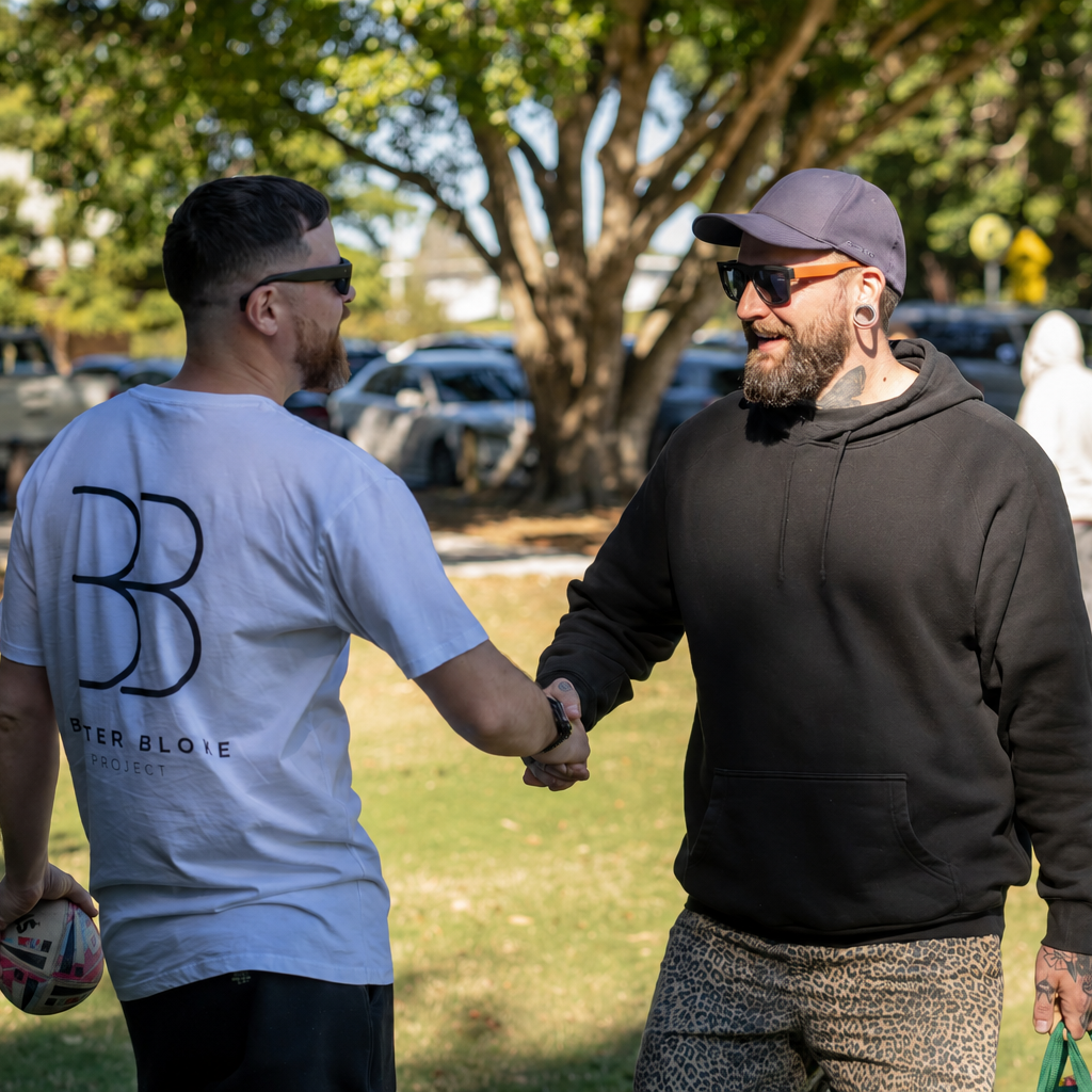 Two men shaking hands outdoors with trees and parked cars in the background